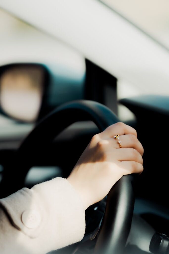 A close-up of a woman's hand on a steering wheel, displaying a ring.